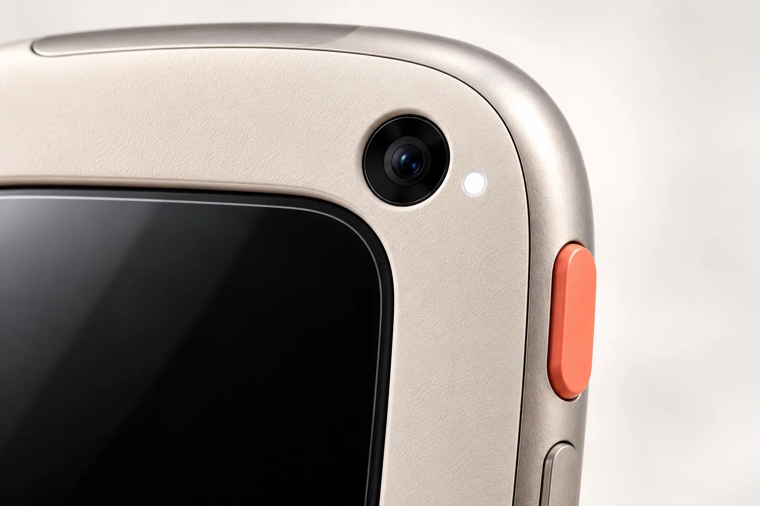 Close up of the top corner: grained shell, titanium-tone frame, the coral button and the edge of the glass